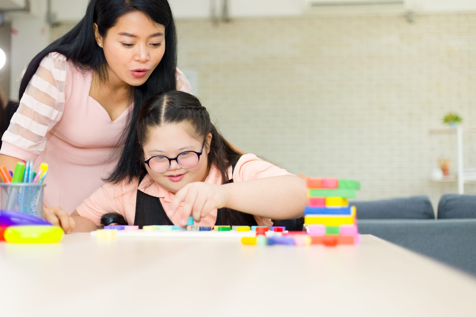 A carer and a young girl building together with colourful blocks — a moment of patient, joyful support.